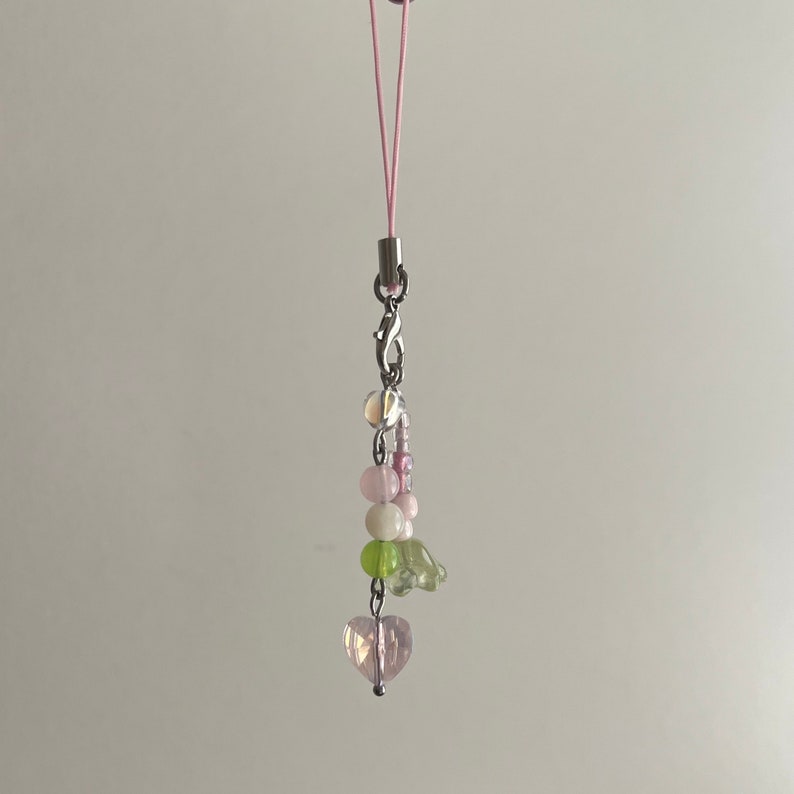 Peut inclure: Un porte-cl&eacute;s de t&eacute;l&eacute;phone en perles roses et vertes avec un charme en forme de c&oelig;ur au bas. Le charme est attach&eacute; &agrave; une ficelle rose.