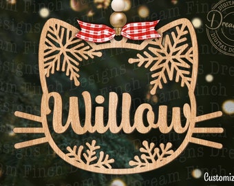 May include: A wooden cutout of a cat's face with snowflakes and the name "Willow" in a decorative font. The cutout is a light brown color and has a red and white checkered bow on top.
