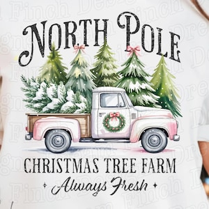 May include: White t-shirt featuring a watercolor design of a pink vintage truck carrying a Christmas tree. The text reads "North Pole Christmas Tree Farm Always Fresh."