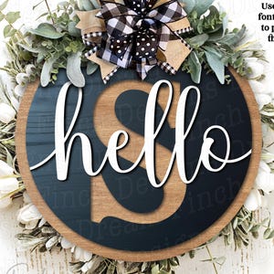 May include: A circular wooden sign featuring the word "hello" in white script. The sign has a navy blue background, a wooden border, and is adorned with greenery and a bow with a black and white checkered ribbon. The text "project idea!" is in the upper right corner.