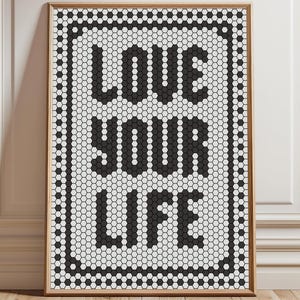 May include: A framed art print with the words "LOVE YOUR LIFE" in bold black letters. The text is set against a white background with a black border, all within a wooden frame. The artwork has a mosaic tile design.