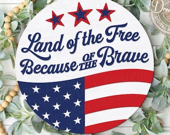 Puede incluir: Un círculo blanco con un diseño de bandera estadounidense roja, blanca y azul. El texto "Land of the Free Because of the Brave" está escrito en letras cursivas azules en el círculo.