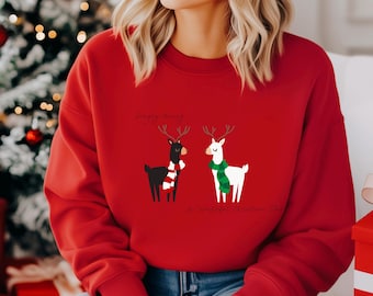 May include: A red sweatshirt featuring two reindeer with scarves. One reindeer is black with a red and white scarf, and the other is white with a green scarf. The text "Simply Merry" and "A Wonderful Christmas Time" are above and below the reindeer.