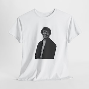 May include: White t-shirt featuring a black and white image of a smiling person. The person is wearing a dark jacket over a white shirt. The t-shirt is made of a soft, lightweight material.