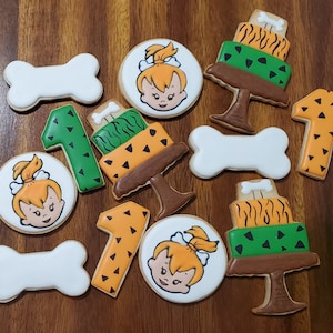 May include: A set of ten decorated sugar cookies featuring cartoon characters and numbers. The cookies are decorated with green, brown, white, and orange icing. The cookies are shaped like bones, numbers, and circles.