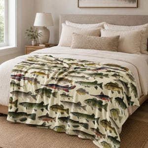 May include: A cream-colored throw blanket featuring a repeating pattern of various fish illustrations in shades of green, brown, red, and blue. The blanket is draped over a bed with neutral-toned bedding.