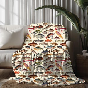 May include: A cream-colored throw blanket with a colorful fish pattern. The blanket features a variety of fish in different colors and sizes, including red, blue, green, yellow, and orange. The fish are arranged in a random pattern on the blanket.