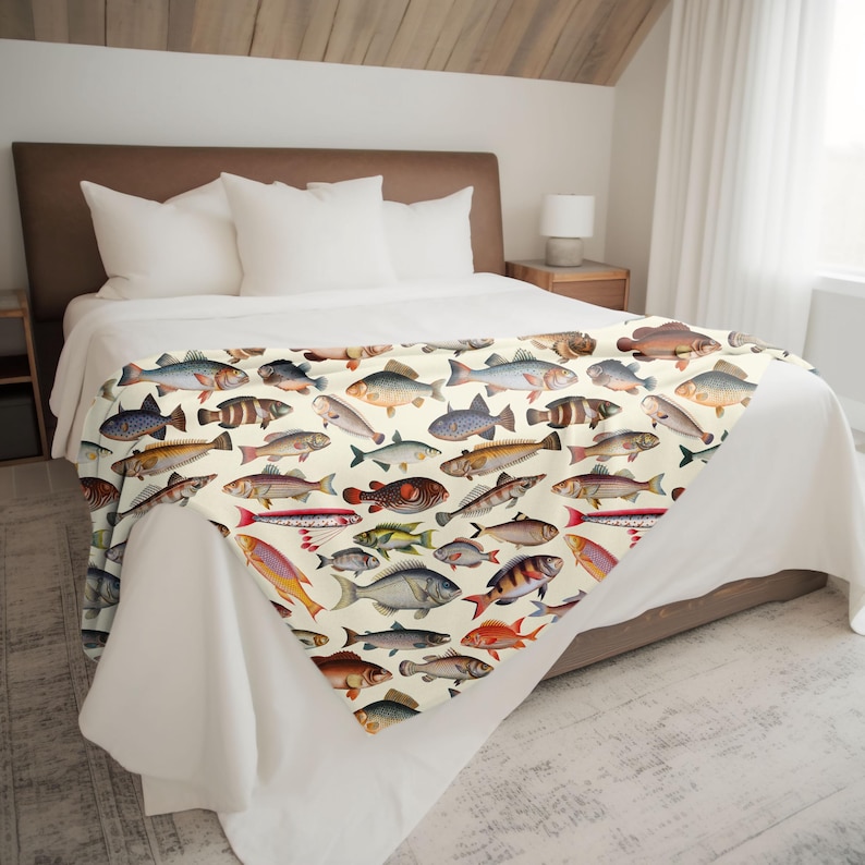 May include: A white throw blanket with a colorful pattern of various fish illustrations. The blanket is folded and displayed on a bed with white bedding.