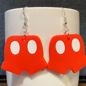 Peut inclure: Une paire de boucles d'oreilles pendantes rouges avec des cercles blancs. Les boucles d'oreilles sont en forme de pantalon.