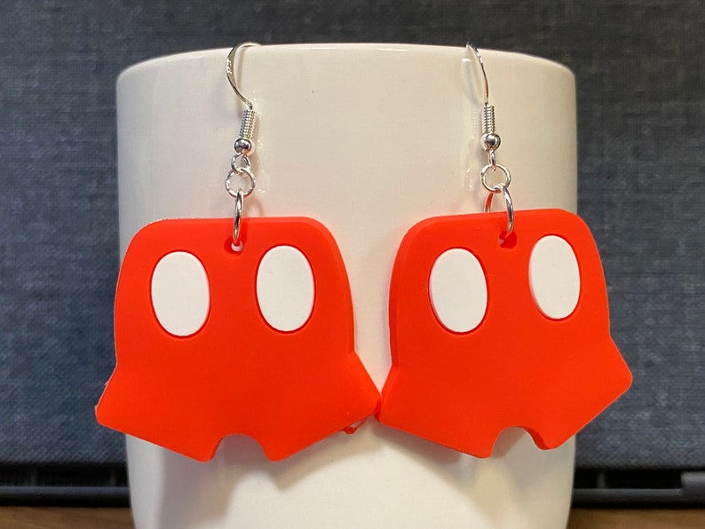 Peut inclure: Une paire de boucles d'oreilles pendantes rouges avec des cercles blancs. Les boucles d'oreilles sont en forme de pantalon.