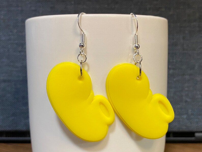 Peut inclure: Une paire de boucles d'oreilles pendantes jaunes en forme d'oreilles de Mickey avec des crochets argent&eacute;s.