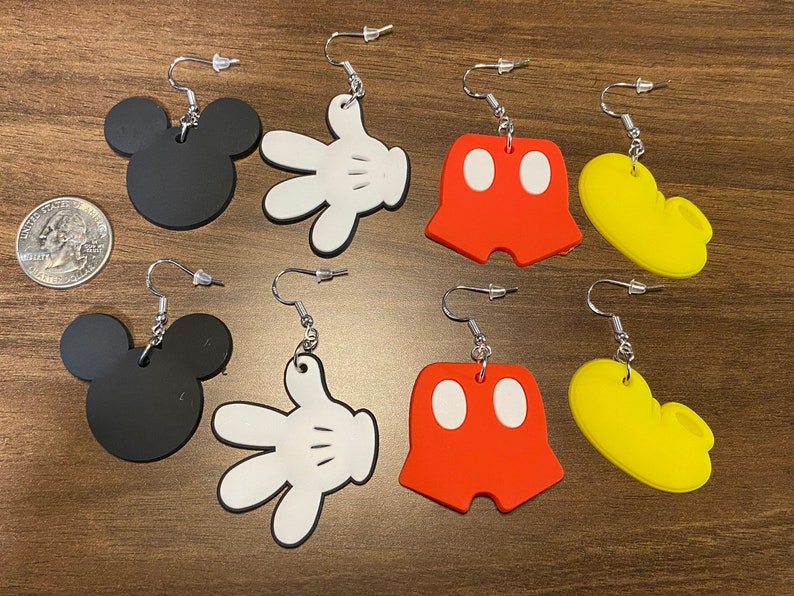 Peut inclure: Six paires de boucles d'oreilles pendantes repr&eacute;sentant diff&eacute;rents personnages embl&eacute;matiques de Mickey Mouse. Les boucles d'oreilles sont en plastique noir, blanc, rouge et jaune. Chaque paire repr&eacute;sente un personnage diff&eacute;rent&nbsp;: la t&ecirc;te de Mickey Mouse, le gant de Mickey Mouse, le short de Mickey Mouse et les chaussures de Mickey Mouse.