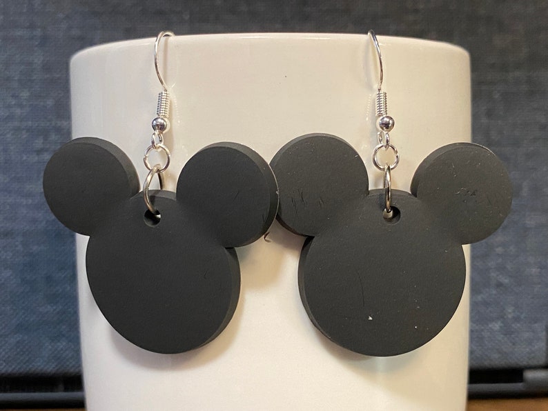Peut inclure: Une paire de boucles d'oreilles noires en forme de t&ecirc;te de Mickey avec des crochets argent&eacute;s.