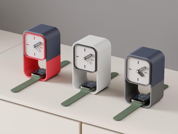 Keephour Watch Stand Clock examples in contrasting colors on a pale cabinet, with watches with green bands shown in the lower spaces.