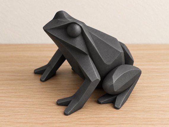 Charcoal frog sculpture, close-up alternate camera angle on pale oak against an ivory wall.
