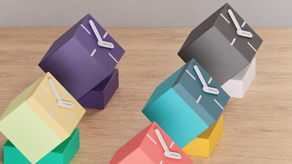 Angled close-up of Tiltblock Cube Desk Clock examples in contrasting colors on light oak against a gray wall.