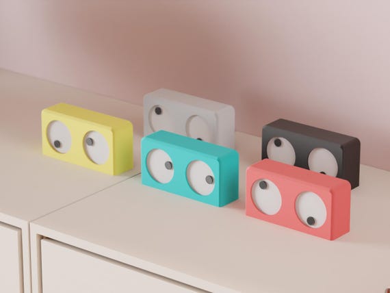 Wander Eyes Desk Clock examples with colorful rectangular bodies, white eyes and dark pupils on a pale cabinet.