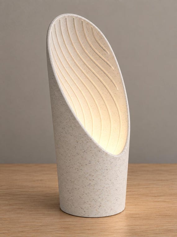 Three-quarter view of the White Marble Cavelle lamp, with fine speckles across the curved shell and interior, gently lit by a battery tea light without a cord.