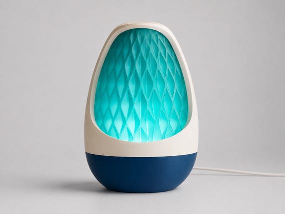 Lumenvale USB lamp in Lagoon, assembled with a Ivory White frame, Marine Blue base and glowing Teal patterned shade on pale gray.