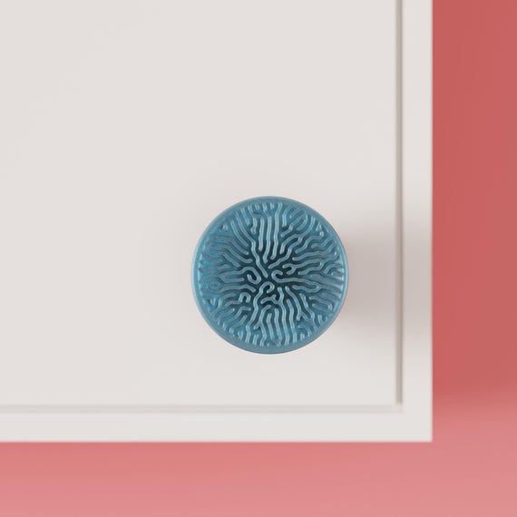 Blue round cabinet knob with branching texture on a white cabinet, close front view.
