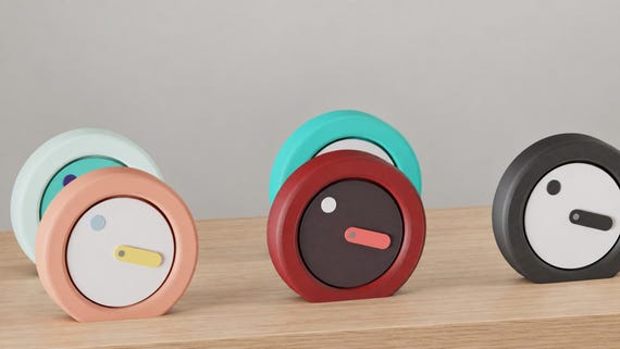 Alternate close-up of Orbitmark Moving Face Clock examples on light oak, showing their colored faces, hands and body profiles.