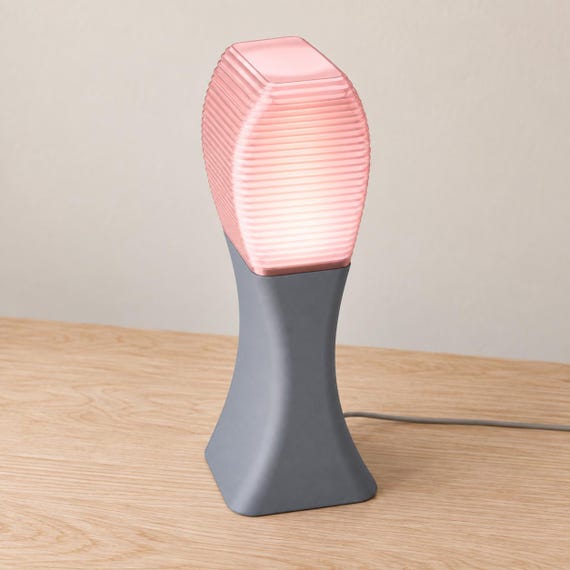 Elevated three-quarter view of the Arcelle lamp in Rose Quartz, with an Ash Gray matte base and Cherry Pink ribbed shade, power cord visible.