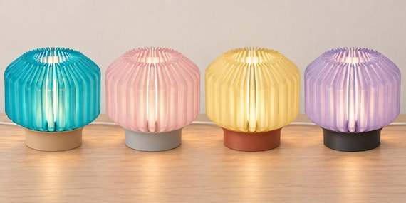 Four illuminated Orivelle lamps on a wood tabletop, left to right: Coastal Cove, Rose Mist, Honey Clay and Lilac Shadow.