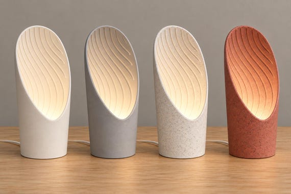 Four Cavelle lamps in Bone White, Ash Gray, White Marble and Red Granite, with warm upward lighting across their wavy interiors and cords behind.