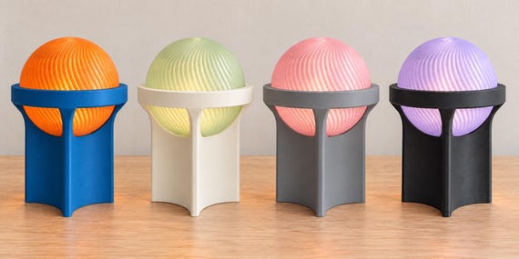 Four cordless Orbessa lamps, left to right: Sunset Cove, Sage Pearl, Rose Slate and Violet Dusk, on a pale wood tabletop.