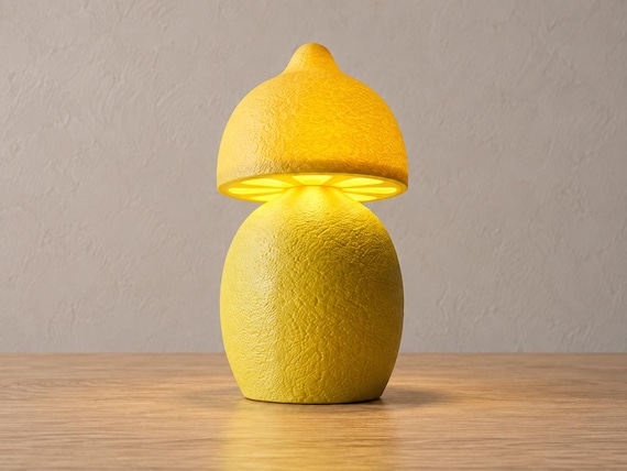 Yellow lemon lamp with textured peel and lifted lemon-shaped shade, close-up three-quarter view on light oak against a pale gray wall.