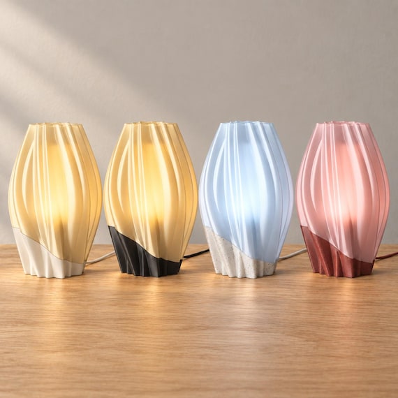 Four wired Orelune lamps on oak, left to right: Linen Halo, Midnight Amber, Marble Mist and Granite Blush, with flowing shades and curved base seams.
