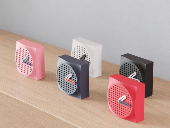 Angled close-up of Dappledial Perforated Desk Clock examples in contrasting colors on light oak against a gray wall.