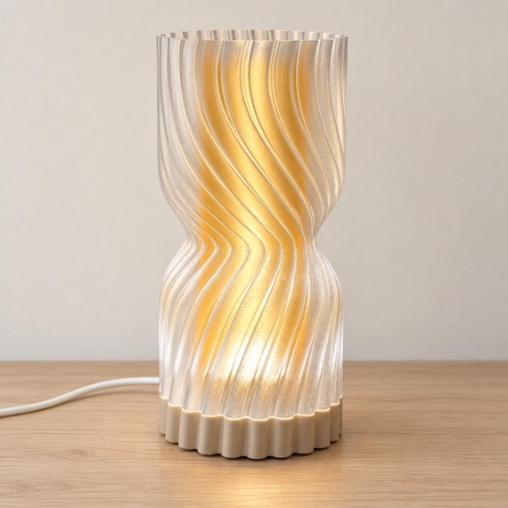 Amber Sand Rillora lamp with a Desert Tan matte base, glowing Mellow Yellow inner diffuser and clear rippled outer shade on a pale wood tabletop.