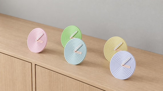 Angled close-up of Rippledot Round Desk Clock examples in contrasting colors on light oak against a gray wall.