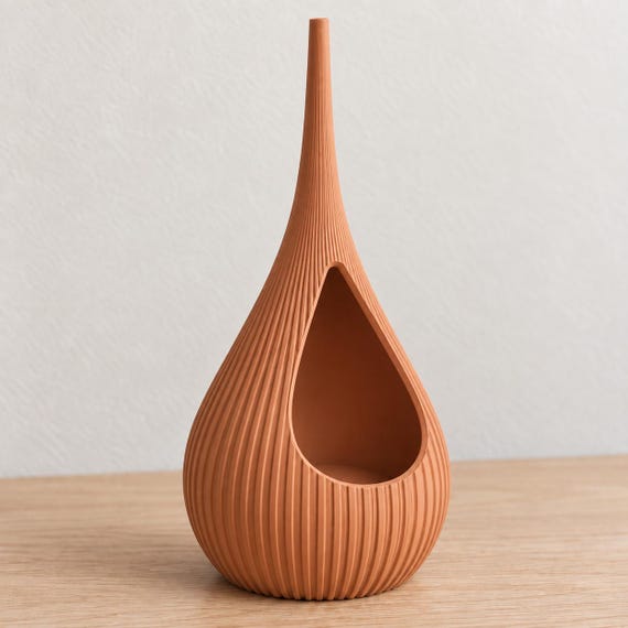 Terracotta Solenne holder alone, showing its empty open cavity, fine vertical ribs and tall tapered neck on a pale wood tabletop.