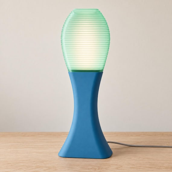 Tidal Mist Arcelle lamp with a Marine Blue matte base and glowing Light Jade ribbed shade on a pale wood tabletop, viewed from the front.
