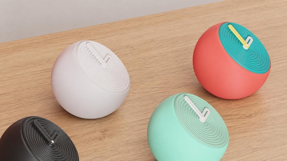 Angled close-up of Pebblewave Spherical Desk Clock examples in contrasting colors on light oak against a gray wall.