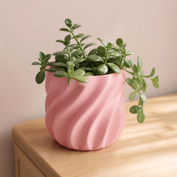Pink CurrentFold sculptural planter with a trailing green plant on a bedside table