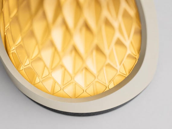 Elevated close-up of the assembled Honeyglow lamp, showing its glowing Mellow Yellow diamond-textured shade, Bone White frame and Charcoal base edge.