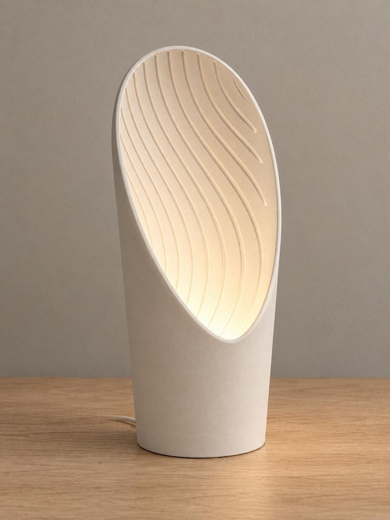 Cavelle lamp in Bone White with a smooth outer shell and wavy curved interior illuminated from below, wired USB cord visible behind on a wood tabletop.