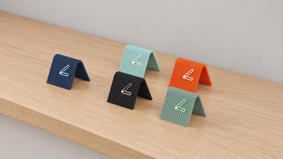 Alternate close-up of Linefold Compact Desk Clock examples on light oak, showing their colored faces, hands and body profiles.