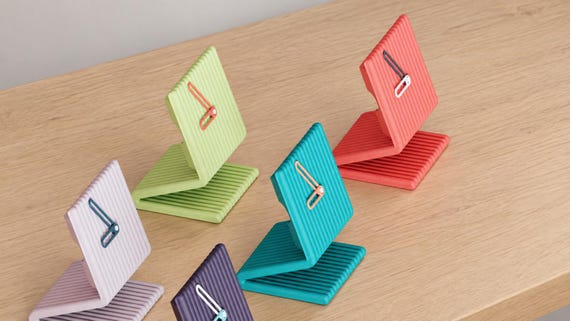 Alternate close-up of Linefold Tall Desk Clock examples on light oak, showing their colored faces, hands and body profiles.