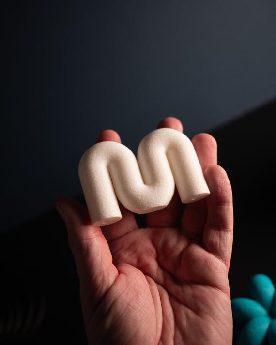 Cream wavy cabinet knob held in a hand, showing the rounded face and curved shape.
