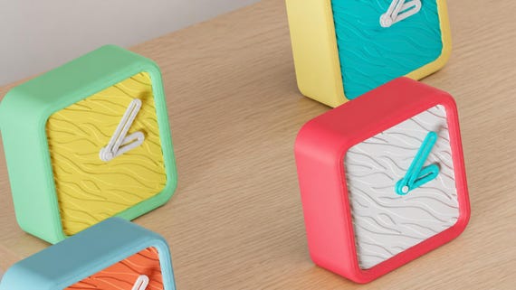 Alternate close-up of Wildline Textured Desk Clock examples on light oak, showing their colored faces, hands and body profiles.
