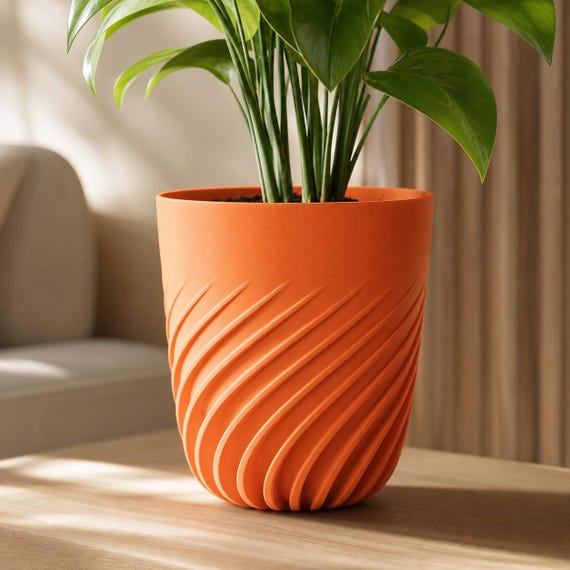 Close-up of a medium Flowspire spiral rib planter in Mandarin Orange with a green plant