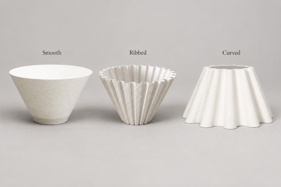 Three ivory white lampshades side by side on a plain warm gray surface, labeled Smooth, Ribbed and Curved, showing their shapes and texture.