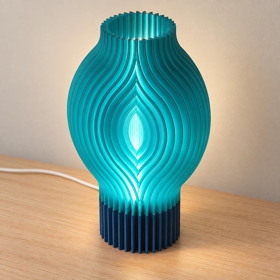 Elevated view of the Tidal Blue Veylora lamp showing its open neck, Teal flowing ribs, illuminated eye-shaped center, Marine Blue base and white cord.