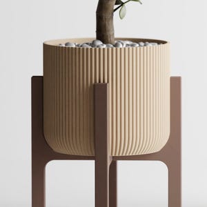 May include: A cylindrical beige planter with a vertical ribbed texture, held by a dark brown wooden stand with four legs. The planter contains a small green plant with rounded leaves and a top layer of small white decorative stones.
