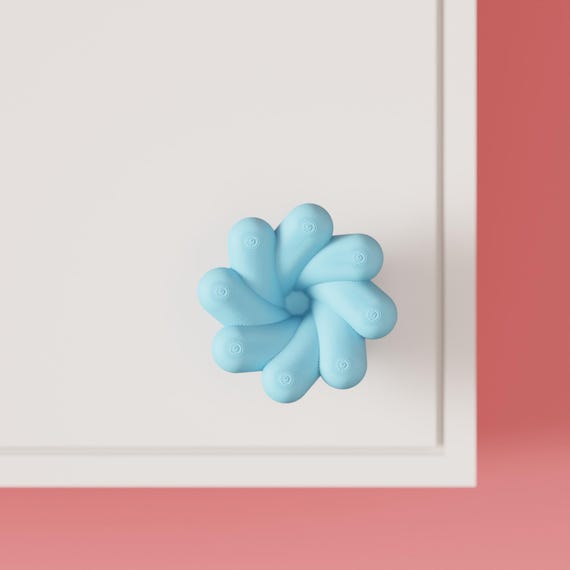 Blue petal-shaped cabinet knob on a white cabinet, close front view.