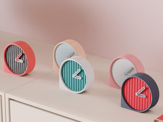 Reedring Round Desk Clock examples in contrasting colors on a pale cabinet, showing the finished clock faces and hands.